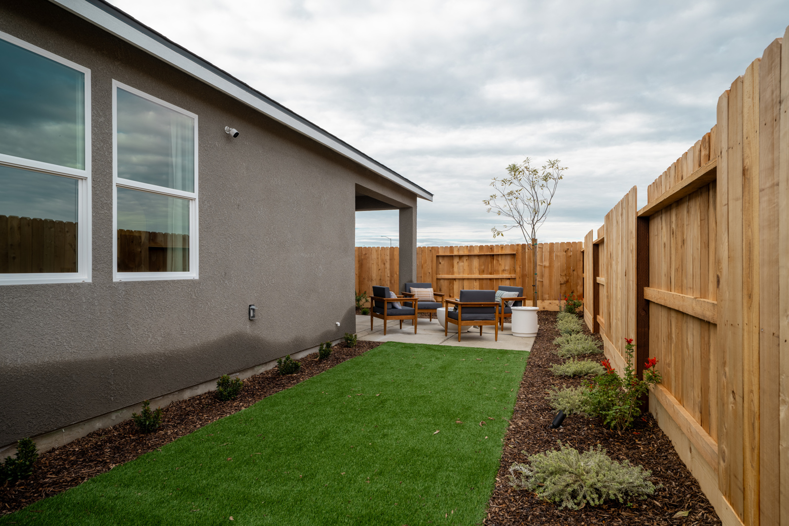A backyard with a fence and a yard with a bench and a tree.