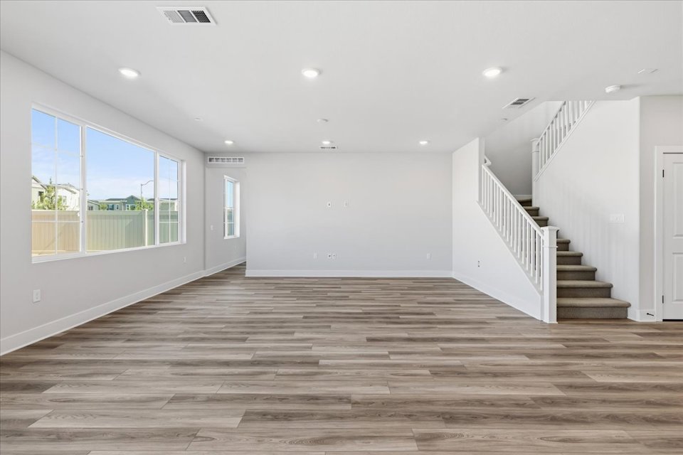 A large empty room with a wood floor and a wood staircase.