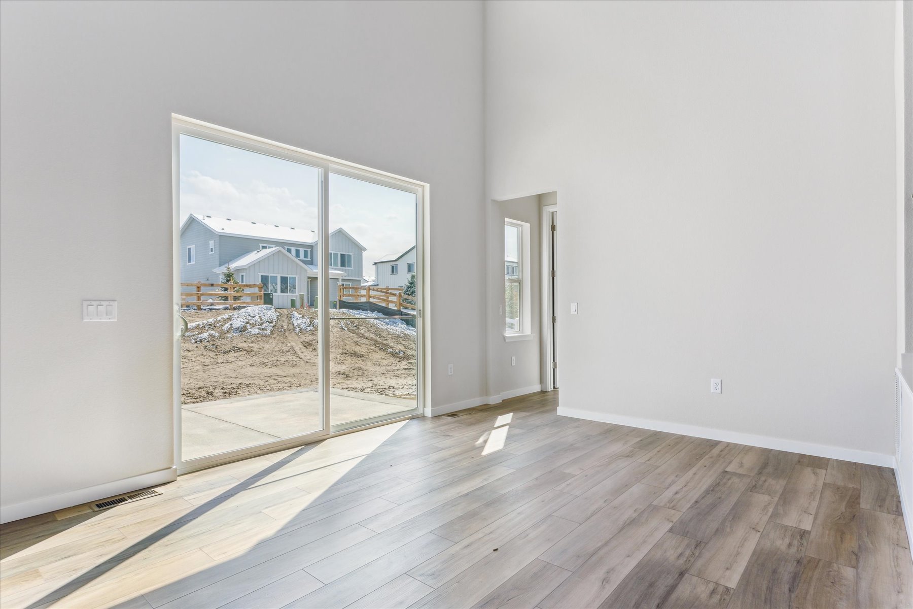 A room with a wood floor and a window with a view of a beach and a building.