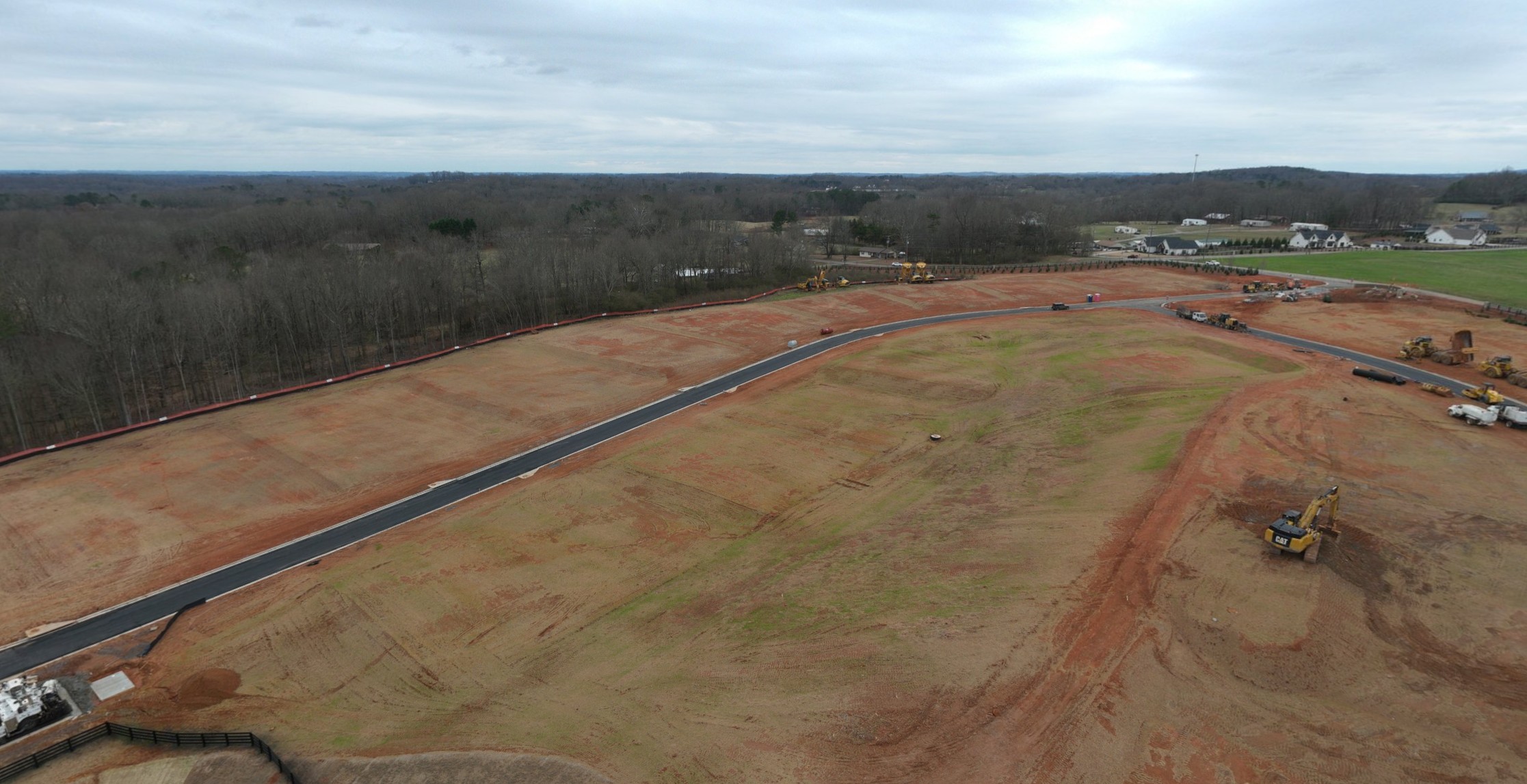 A road with a dirt field and trees on the side.