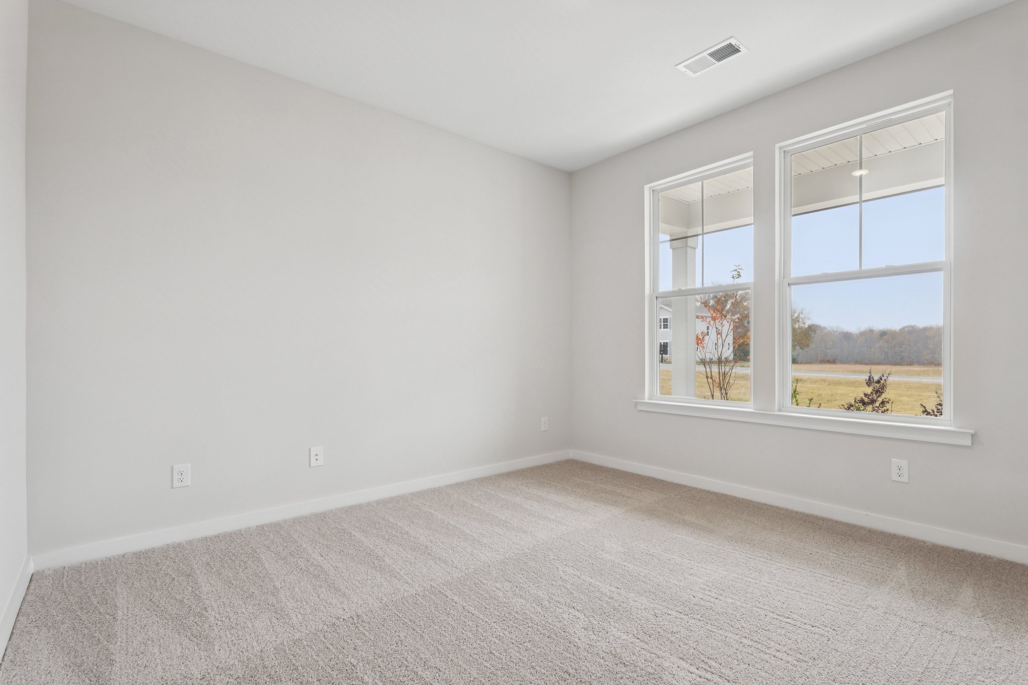 A room with a window and a white wall with a view of a field and trees.