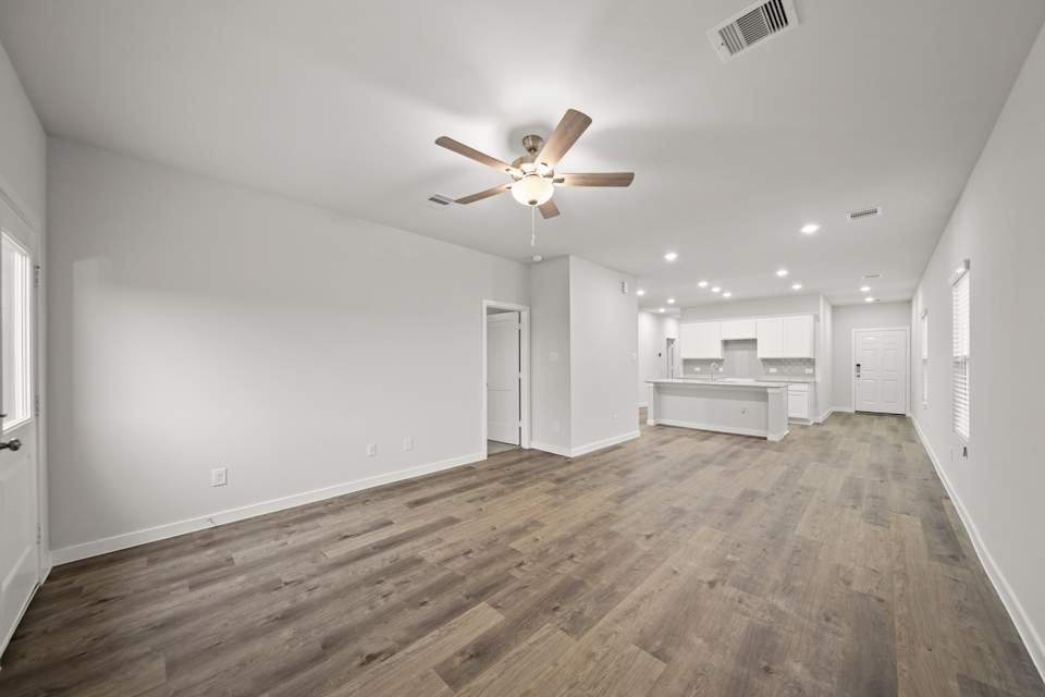 A large empty room with a ceiling fan and wood floors.