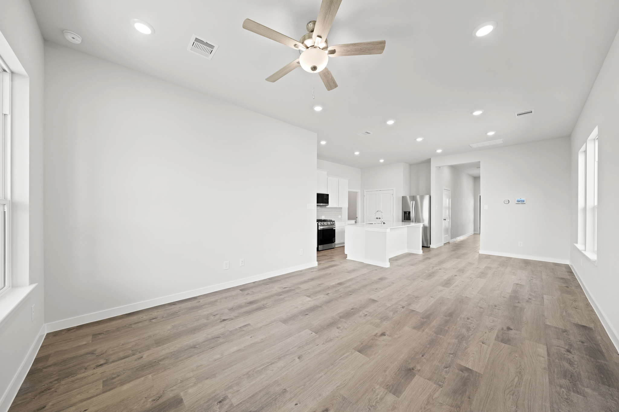 A large empty room with a ceiling fan and a wood floor.