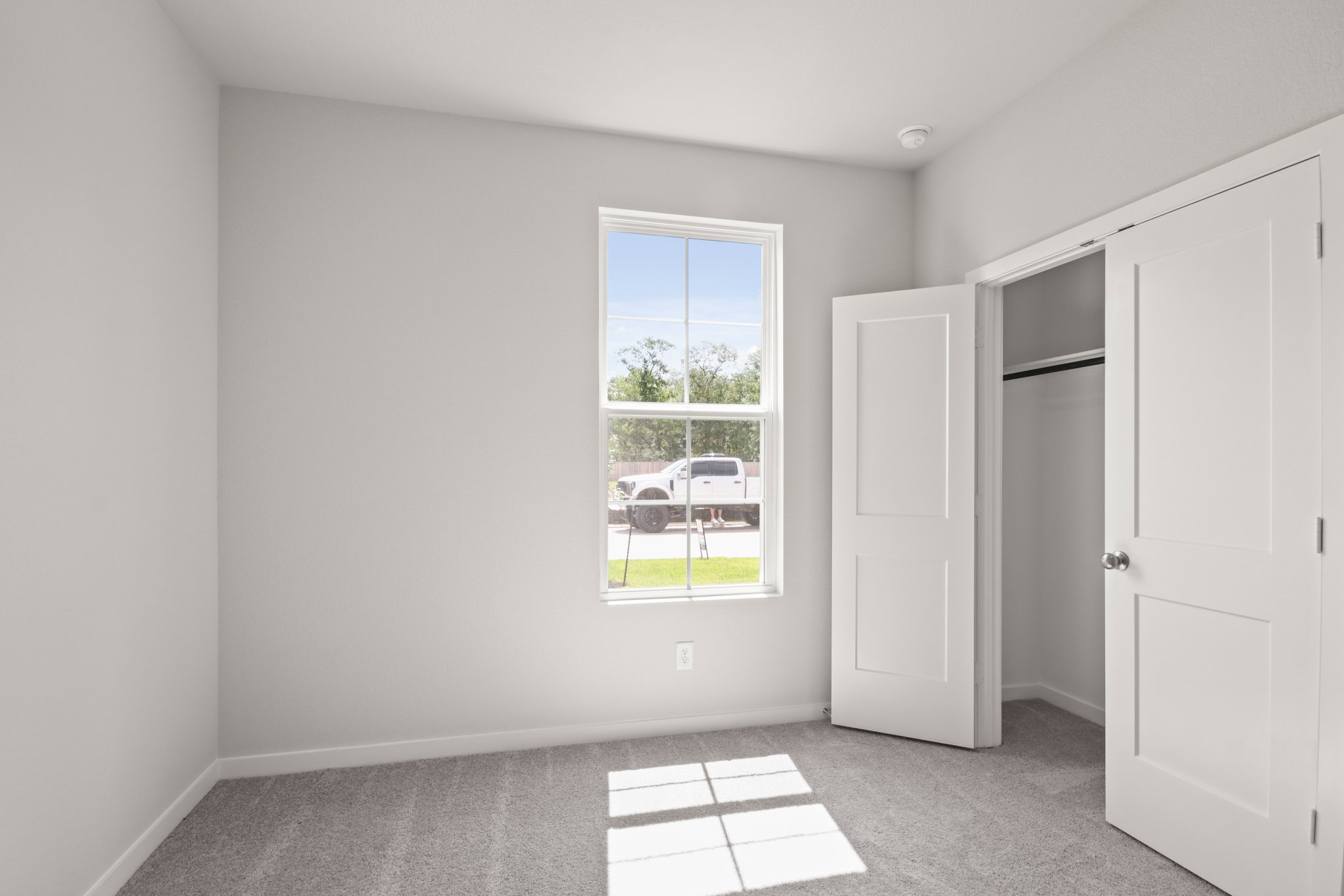 A room with white walls and a window with a car outside.